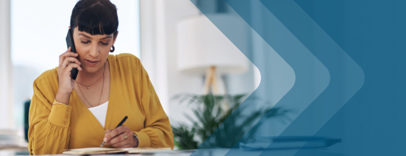 Woman in mustard yellow blouse on phone writing on paper