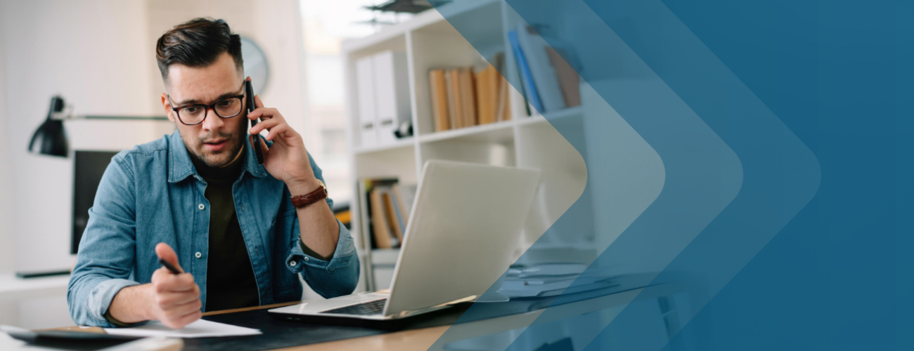 Man wearing glasses talking on his cell phone at his desk