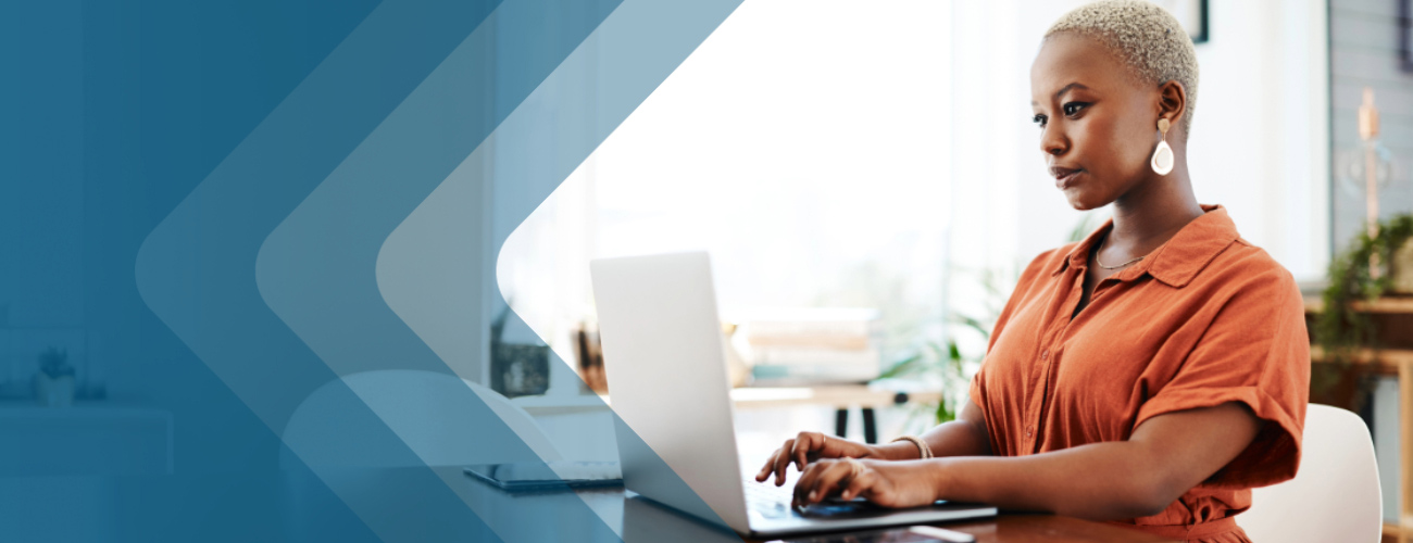 Woman with blonde hair and orange blouse typing on her laptop