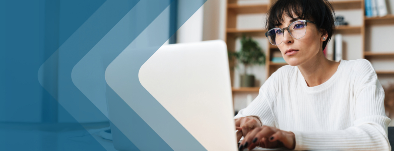 Woman wearing classes sitting at a desk and typing on a laptop.