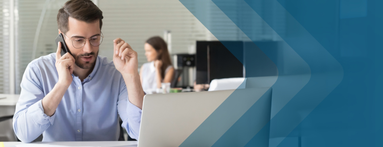 A man on the phone, sitting at a desk in front of a computer.