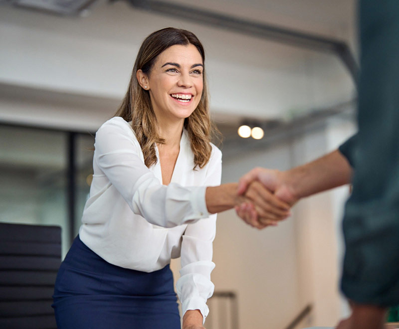 Photo of a woman in an office standing up to shake someone's hand.