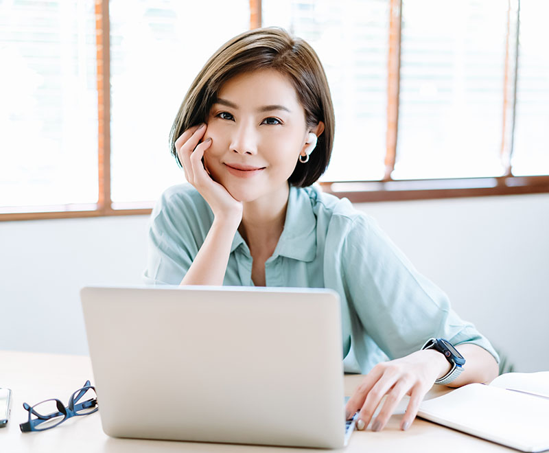 Woman sitting at her desk smiling with her head on her hand