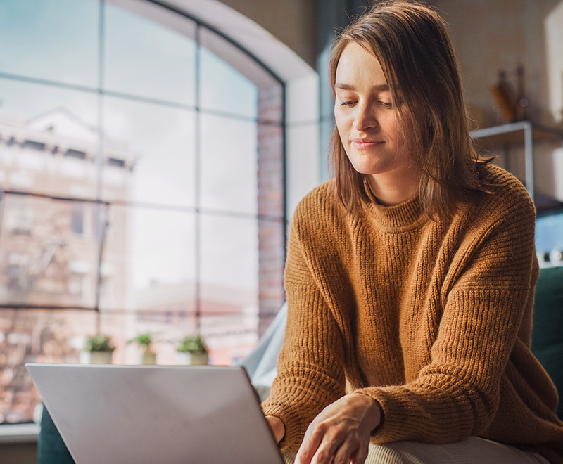 Woman wearing brown sweater smiling typing on her laptop