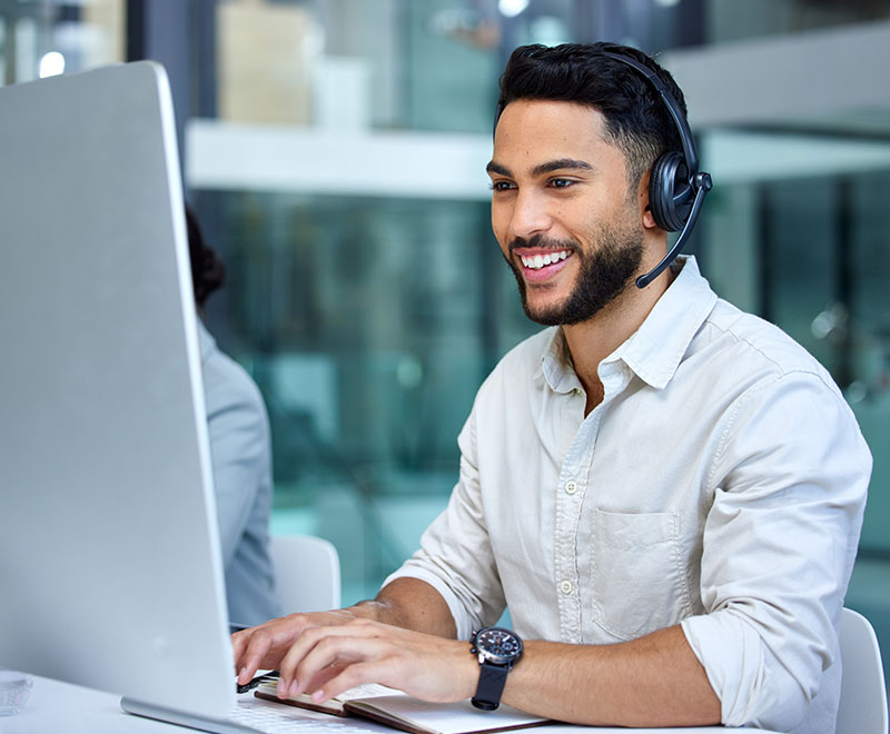 Man wearing a collared shirt smiling and typing at his laptop