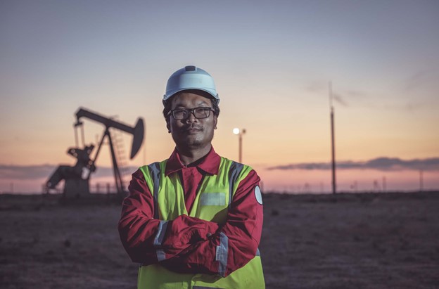 A man wearing a hard hat and yellow vest standing in front of an oil drill.