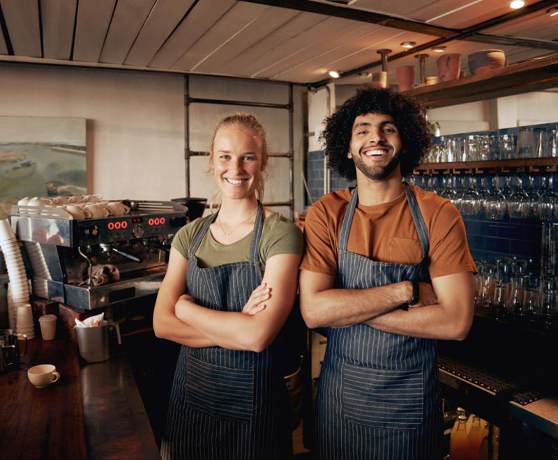 Young man and woman in a coffee shop smiling with arms crossed