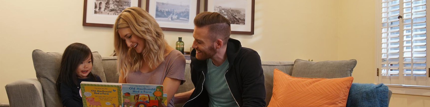 A mother, father, and daughter sitting on a coach reading the book "Old MacDonald Had a Farm."